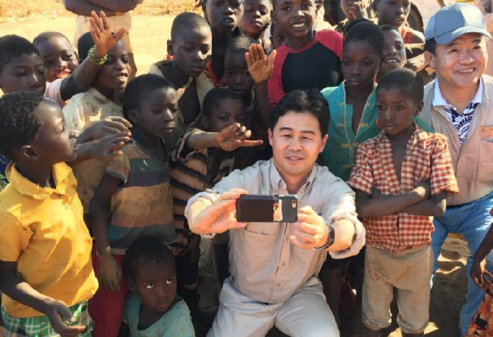 Nu Skin employee takes a selfie with a large group of Malawi children behind him posing for a picture.
